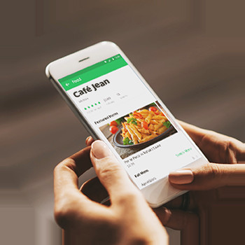 Một người phụ nữ trẻ đang đặt đồ ăn GrabFood trên máy tính xách tay với điện thoại bên cạnh