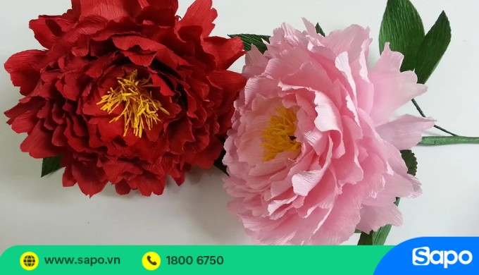 Một bông hoa mẫu đơn màu hồng nhạt làm từ giấy nhún, với các cánh hoa xếp lớp tinh xảo, trông sống động như thật
